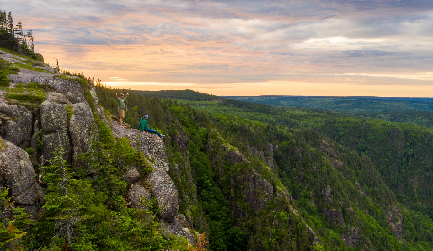 two hikers perch on rocky outcrop looking over the forest