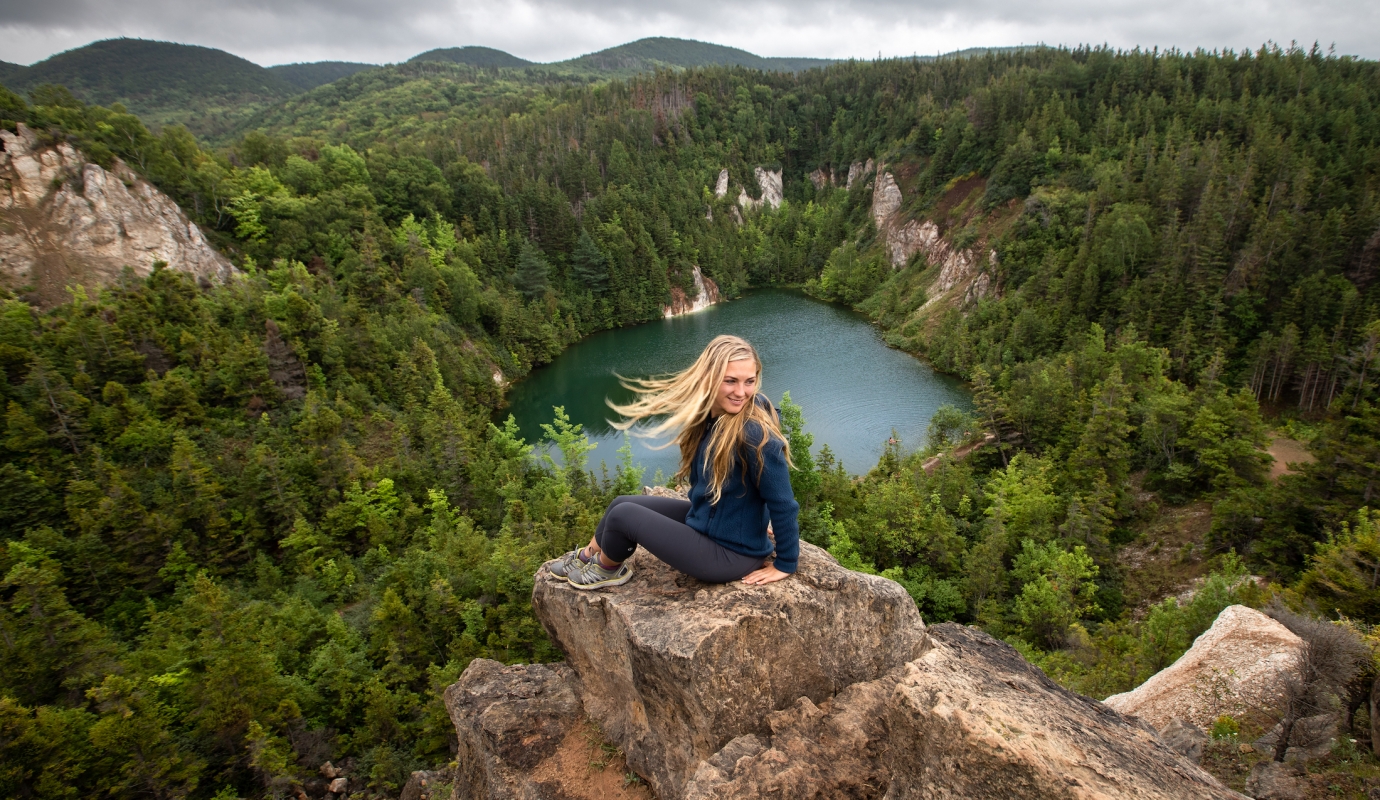 woman sits on rock overlooking lake surrounded by forest