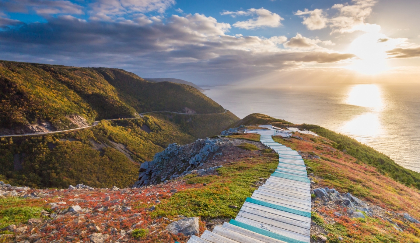 A wooden trail winds down a mountain overlooking the ocean at sunset