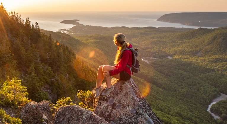 lone hiker sits on rocky outcrop admiring the sunset