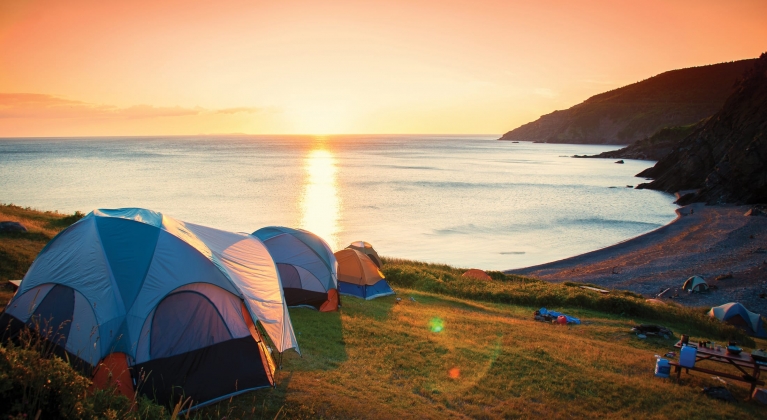 Multiple tents pitched on a hill overlooking the ocean at sunset