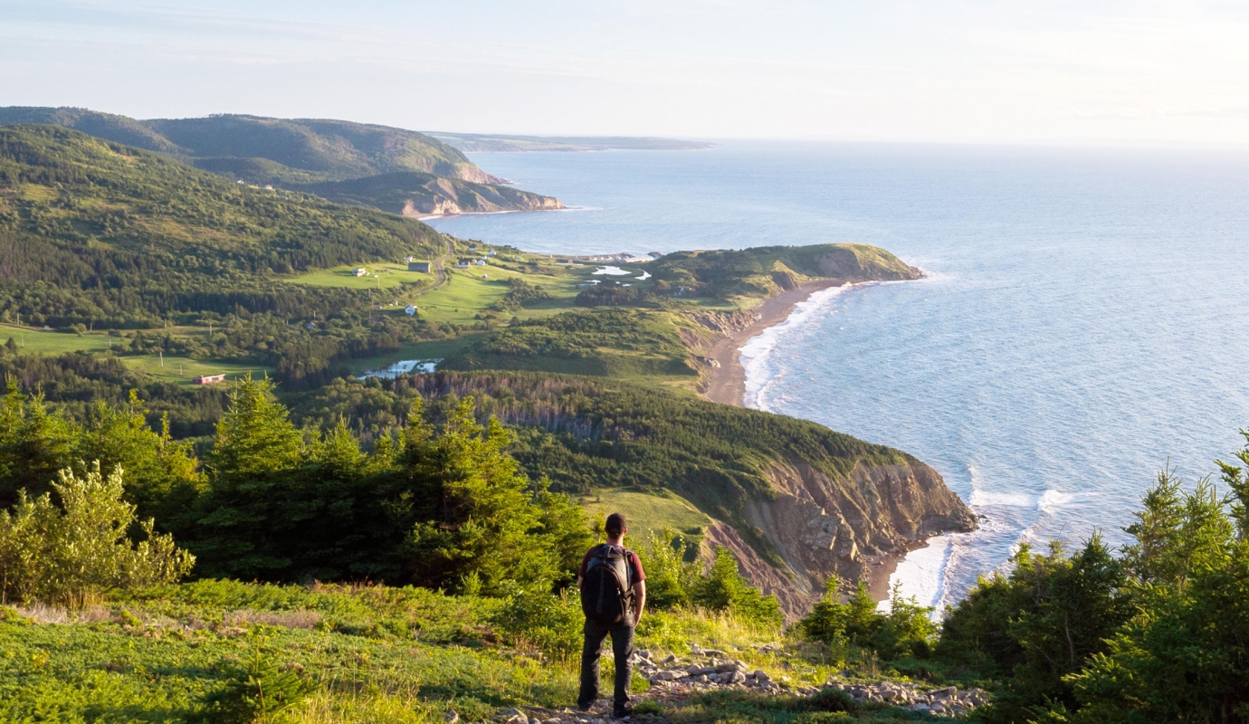 A hiker stands on a grassy hill overlooking the ocean