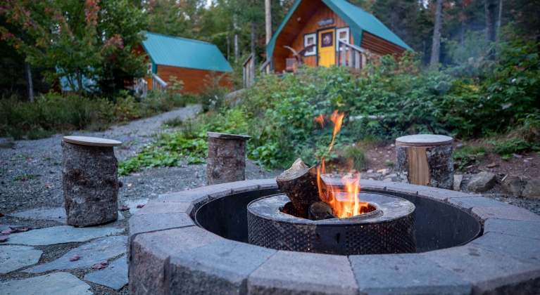 stone fire pit blazes in front of wooden cottages