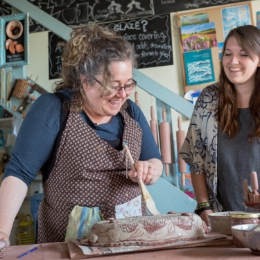 Two smiling women make pottery