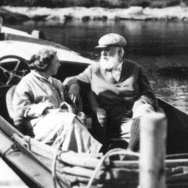 A dated black and white photo of an elderly couple on a boat, having a conversation.