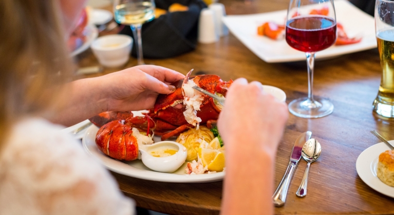 Over the shoulder view of a woman buttering her lobster dinner.